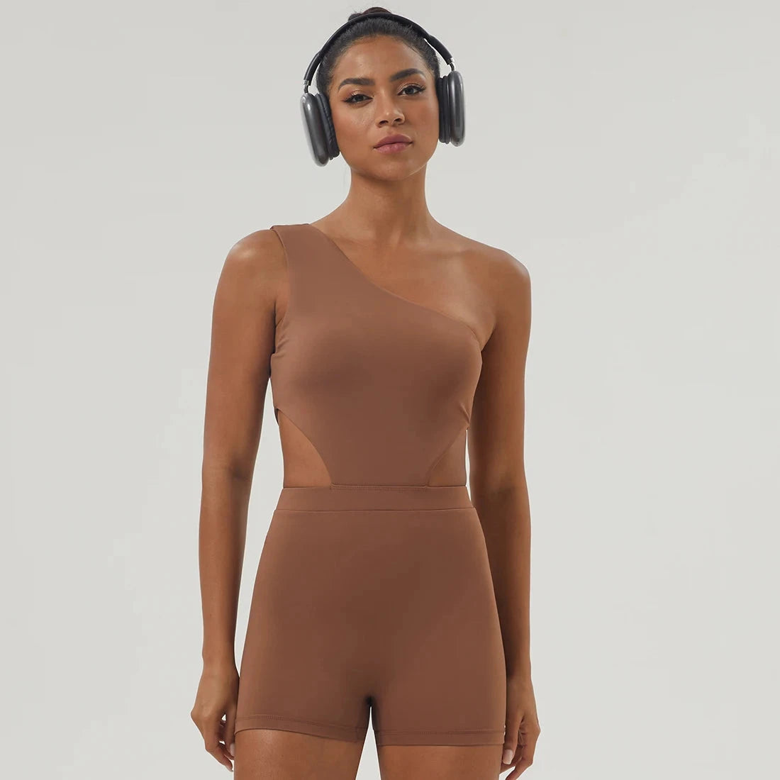 "Brown Women One-Shoulder Sport Bodyduit Jumpsuit with headphones, featuring padded bust and cutout sides for stylish workouts."