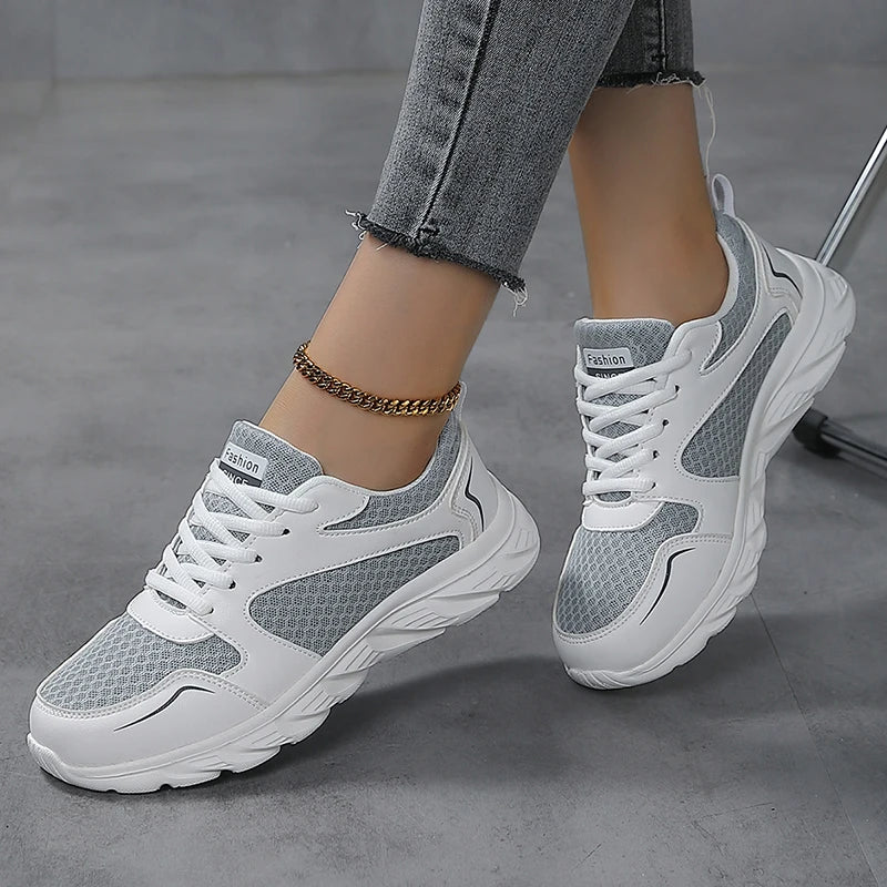 White and gray chunky platform sneakers with mesh panels, shown on a model wearing gray jeans and a gold anklet against a gray concrete floor.