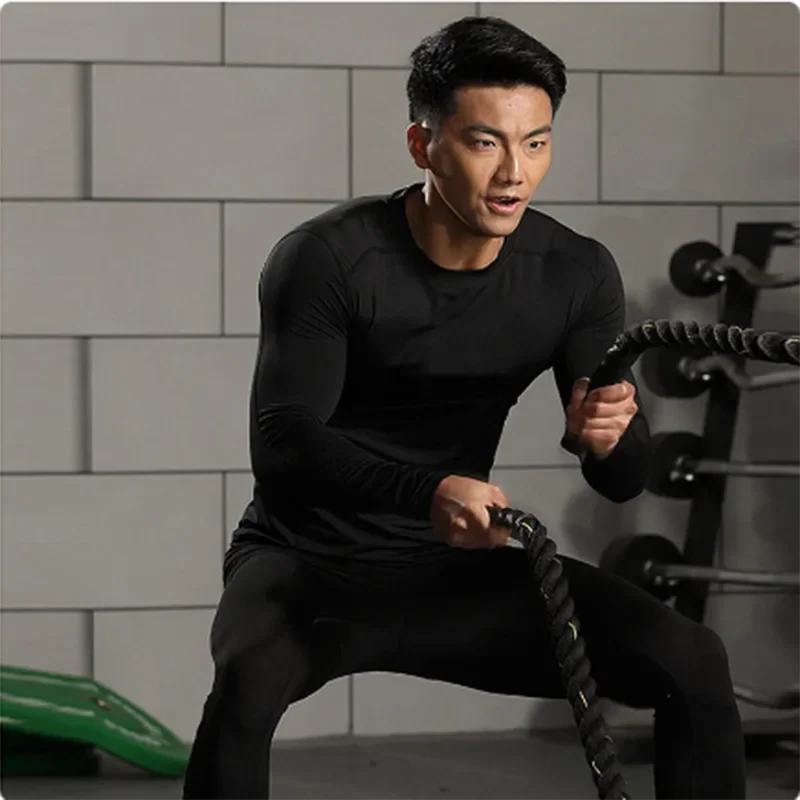 Man using battle ropes wearing black Men's Sports Suit Running fitne male Quick drying Sportswear Compression Clothing Fitness Training kit.
